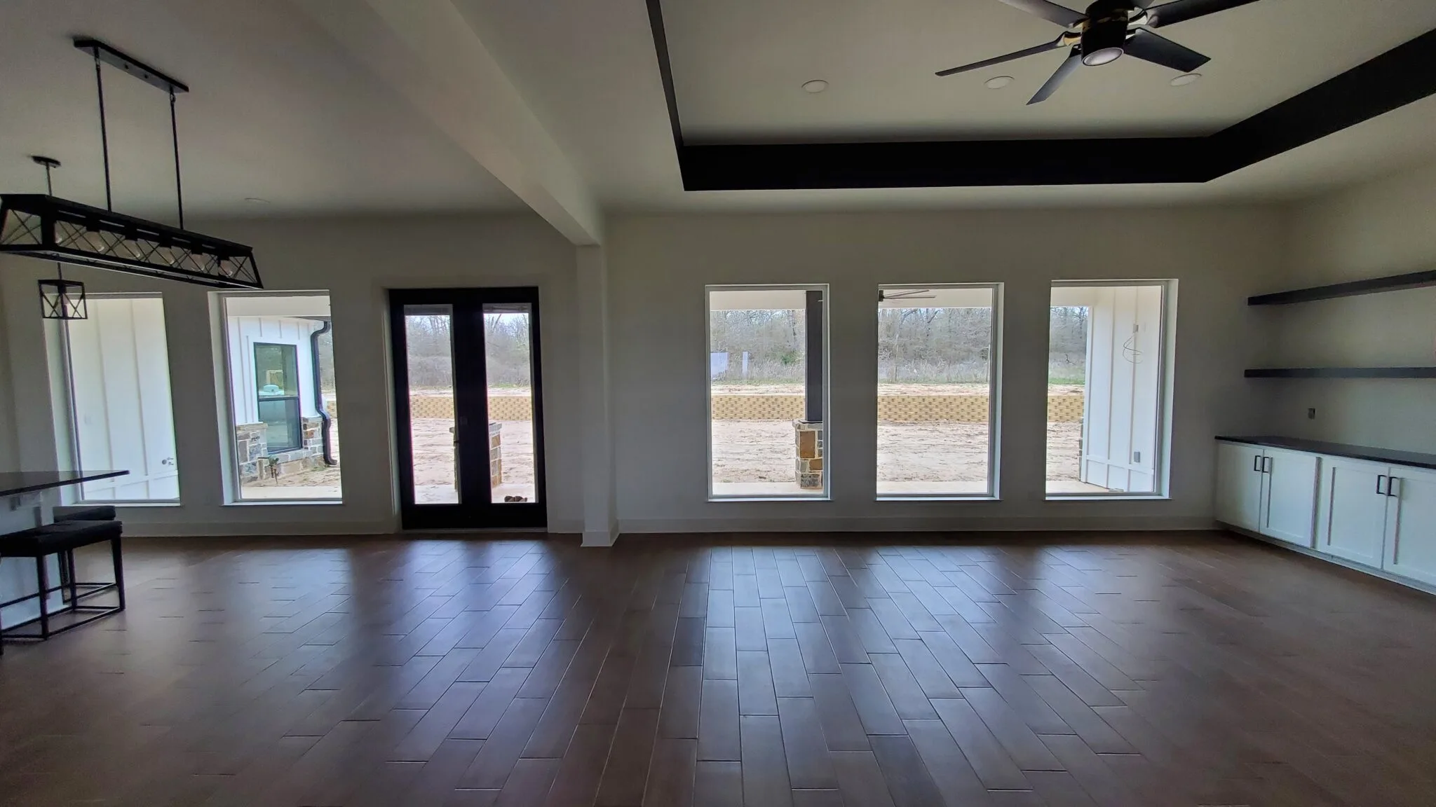 Empty new addition with wood floors, a tray ceiling, ceiling fan and French doors
