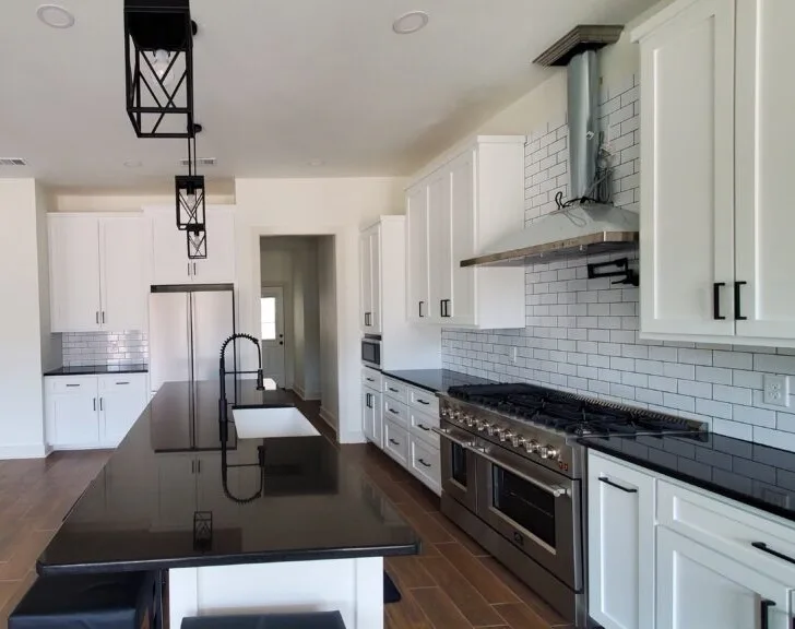 White kitchen with black countertops, a long island and a stainless steel range