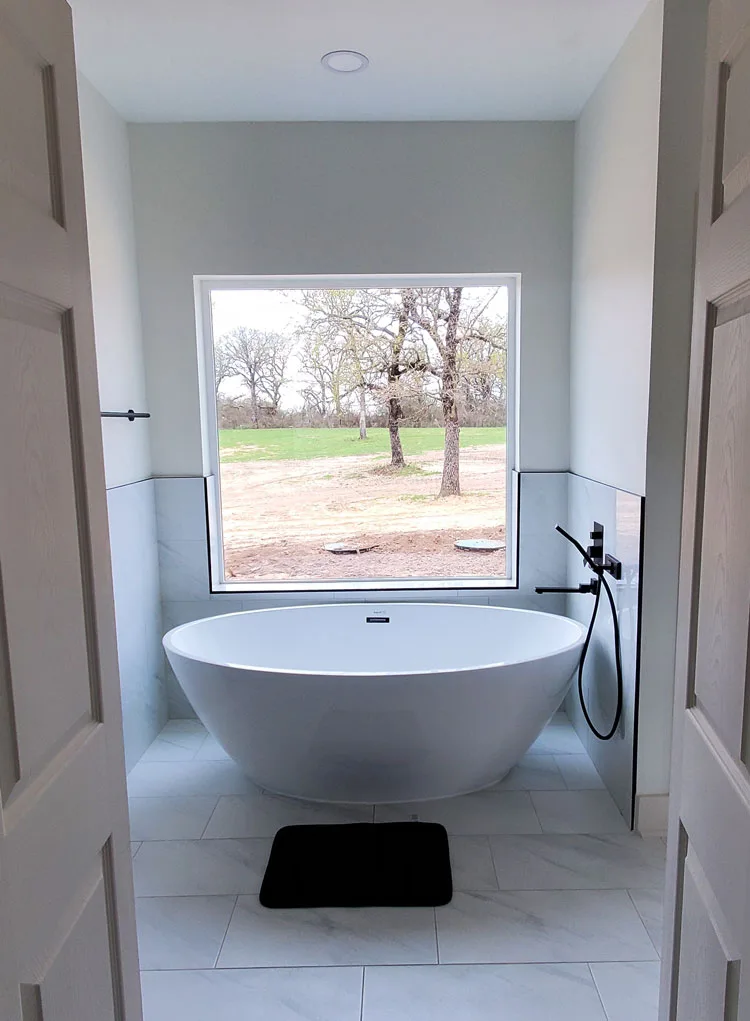 Freestanding white bathtub beneath a large window in a new home
