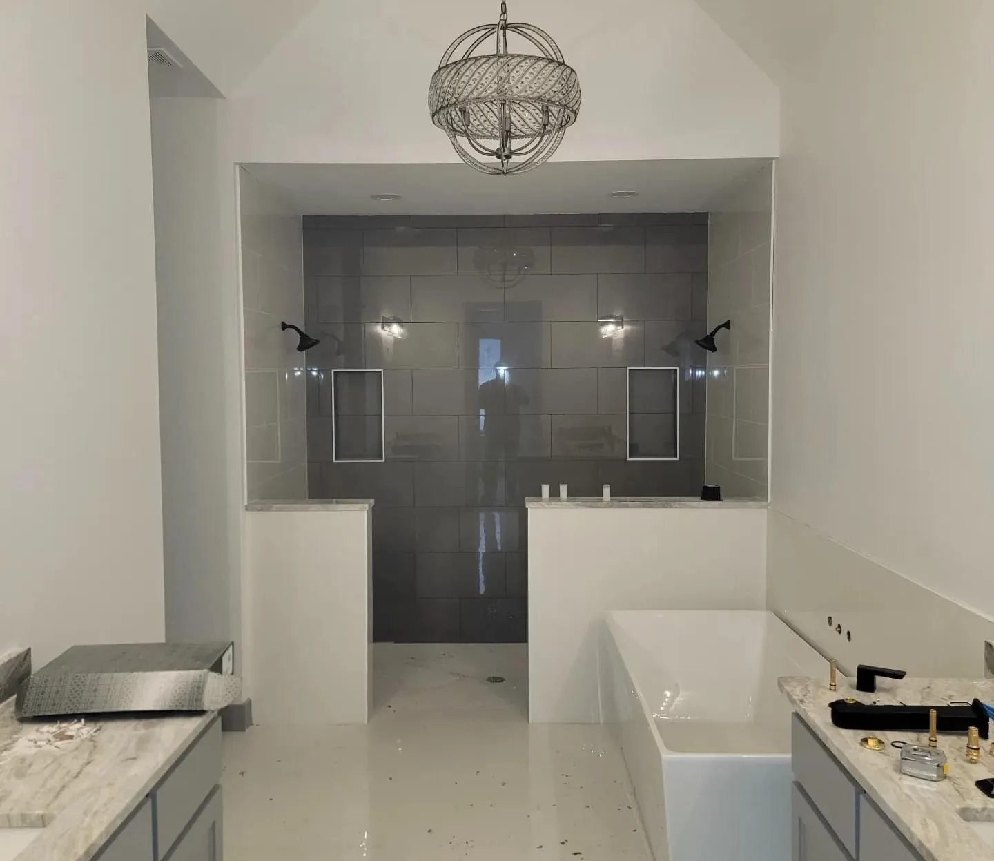 Bathroom remodel in progress with a grey-tiled walk-in shower, chandelier and soaking tub