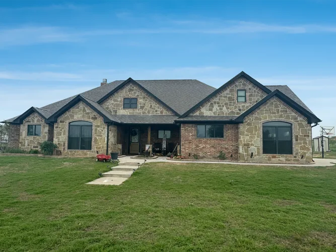 Stone and brick single-storey new home with a green front lawn