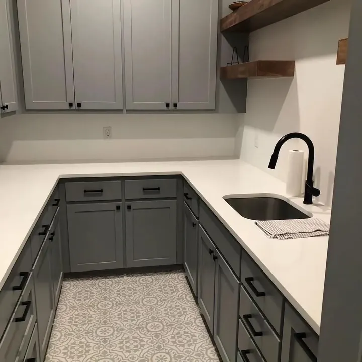 Grey cabinets with a white countertop, undermount sink and black faucet